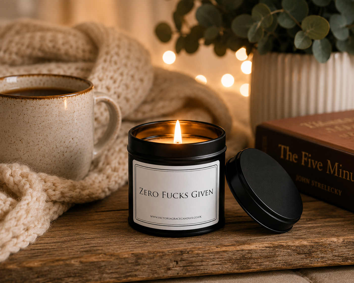 Luxury black soy wax candle beside a cosy blanket, hot drink and warm fairy lights, creating the perfect relaxing evening atmosphere.