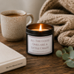 Luxury soy wax candle displayed on a rustic wooden coffee table beside a mug of coffee, cosy knitted blanket, journal and eucalyptus.