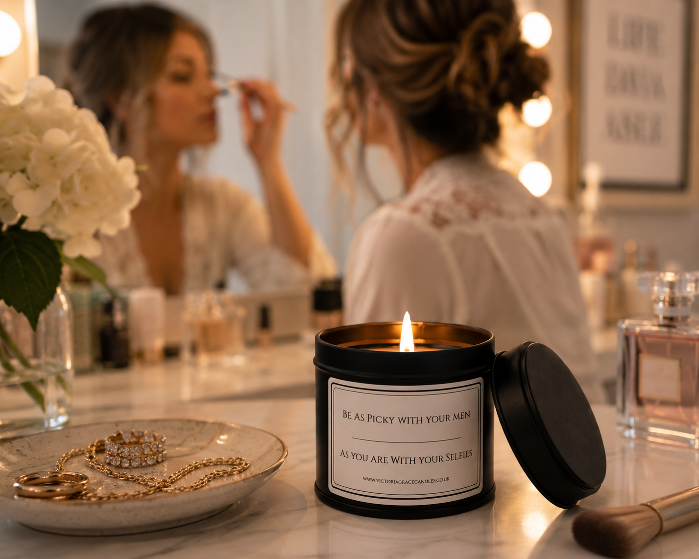 Black tin candle with the word be as picky with your men as you are with your selfies on it in a dressing room environment with a lady putting makeup on in the background.