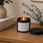 Luxury black soy wax candle displayed on a wooden sideboard with eucalyptus, books and neutral home décor in a peaceful modern interior.