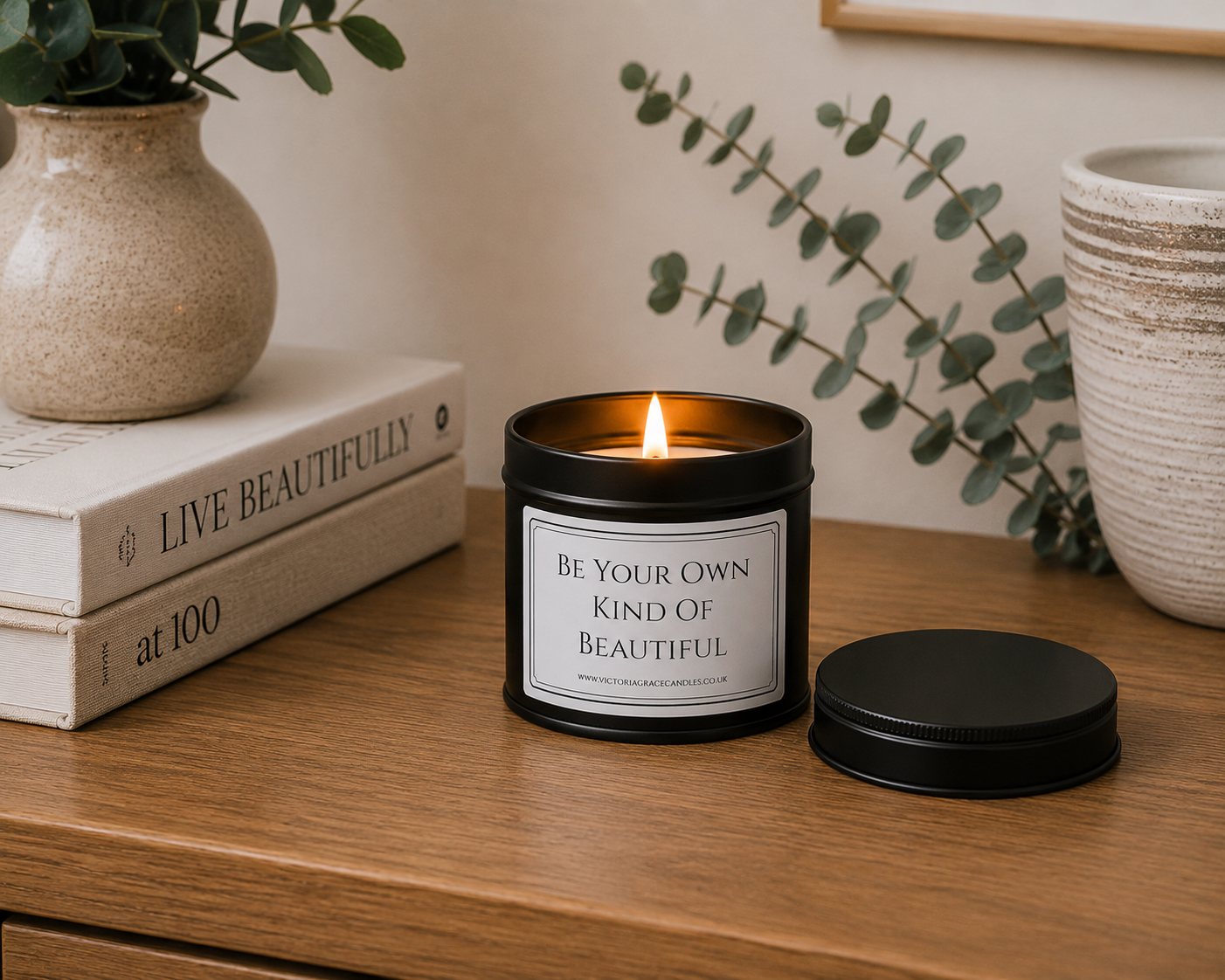 Luxury black soy wax candle displayed on a wooden sideboard with eucalyptus, books and neutral home décor in a peaceful modern interior.