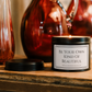 Luxury inspirational soy wax candle displayed on a rustic wooden table with warm amber glass vases, creating a calm and elegant atmosphere.