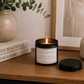 Luxury black soy wax candle displayed on a wooden sideboard with eucalyptus, decorative books and neutral home décor in a modern, calming interior.