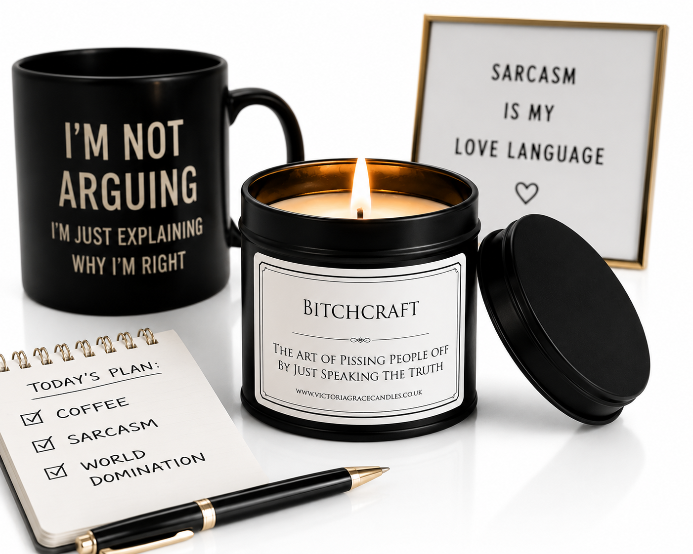 A curated product arrangement on a white background featuring a black candle tin with a lit flame and black lid, a black mug with gold text, a small notepad, a pen, and a framed sign reading 'SARCASM IS MY LOVE LANGUAGE'.