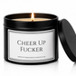 A black metal candle tin with a lit flame and the lid leaning against it on a white background. The front label reads 'CHEER UP FUCKER' with the website VictoriaGraceCandles.