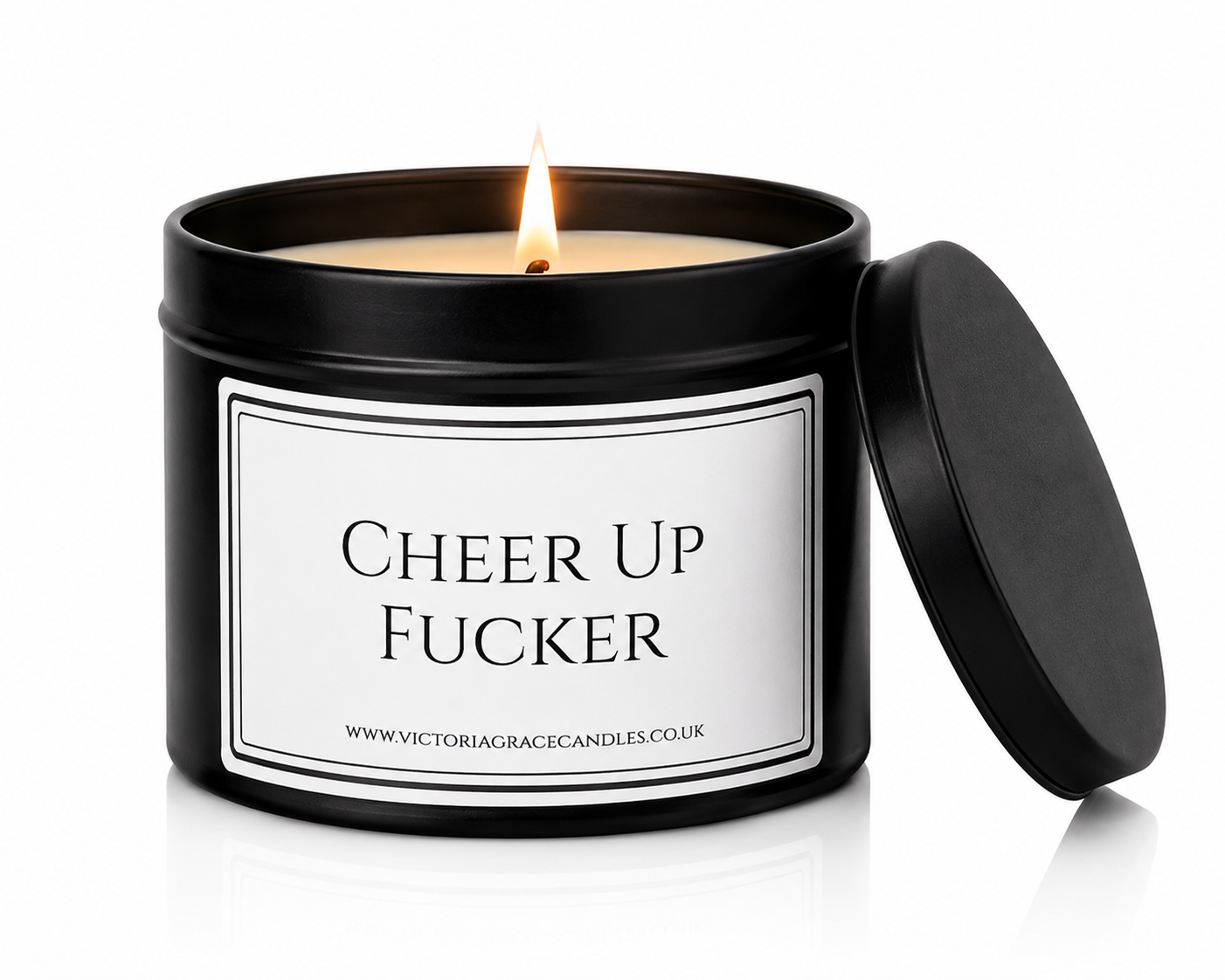 A black metal candle tin with a lit flame and the lid leaning against it on a white background. The front label reads 'CHEER UP FUCKER' with the website VictoriaGraceCandles.