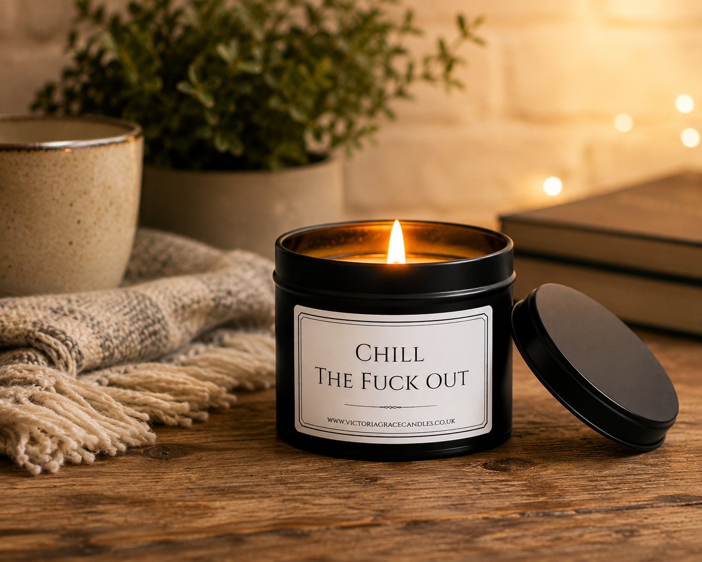 Luxury black soy wax candle beside a cosy blanket, mug and warm ambient lighting, creating the perfect relaxing evening setting.