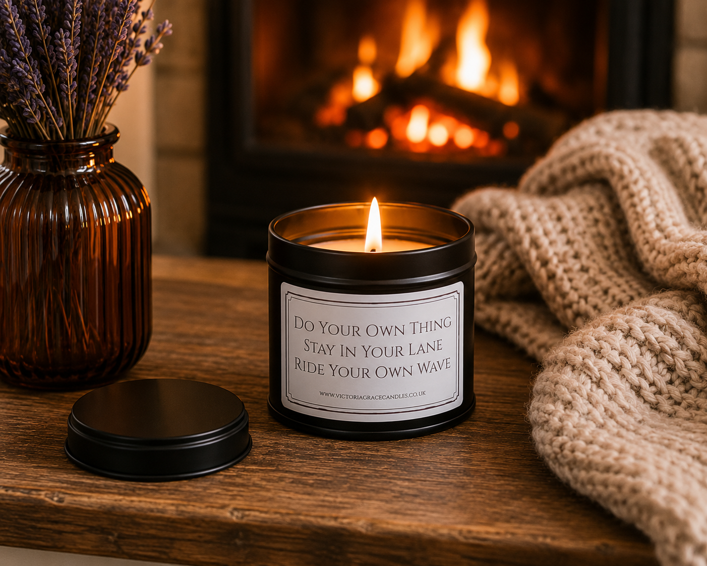 Luxury inspirational candle beside a glowing fireplace with a chunky knitted blanket and amber glass vase, creating a warm and cosy setting.