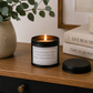 Luxury black soy wax candle displayed on a modern wooden sideboard with eucalyptus, decorative books and neutral home décor in a stylish contemporary interior.
