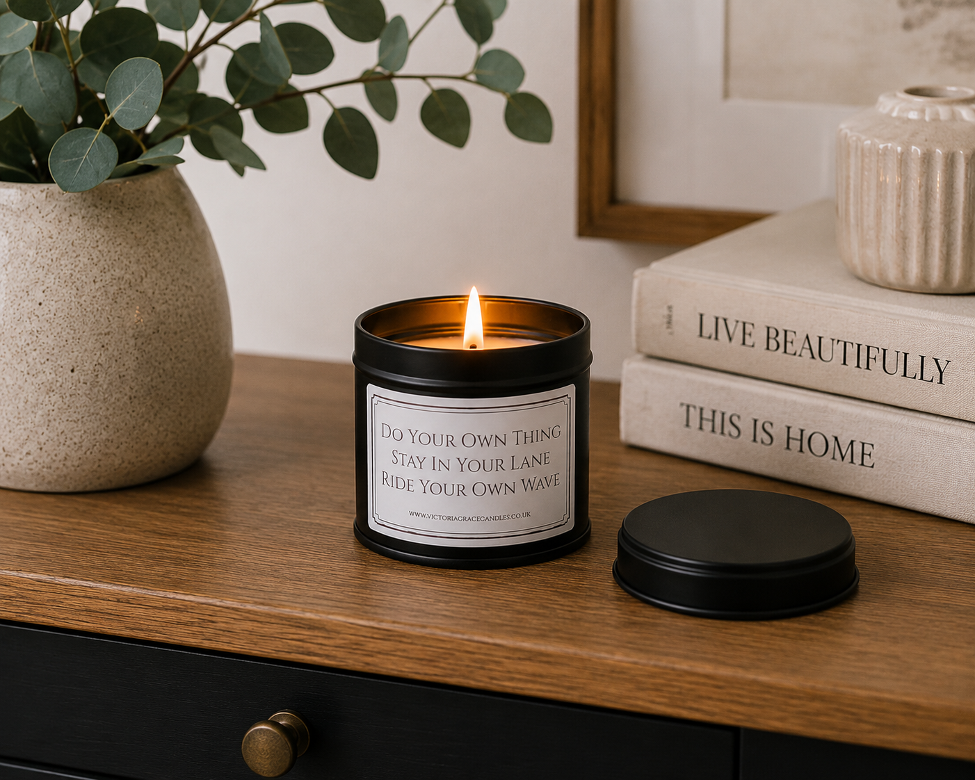 Luxury black soy wax candle displayed on a modern wooden sideboard with eucalyptus, decorative books and neutral home décor in a stylish contemporary interior.