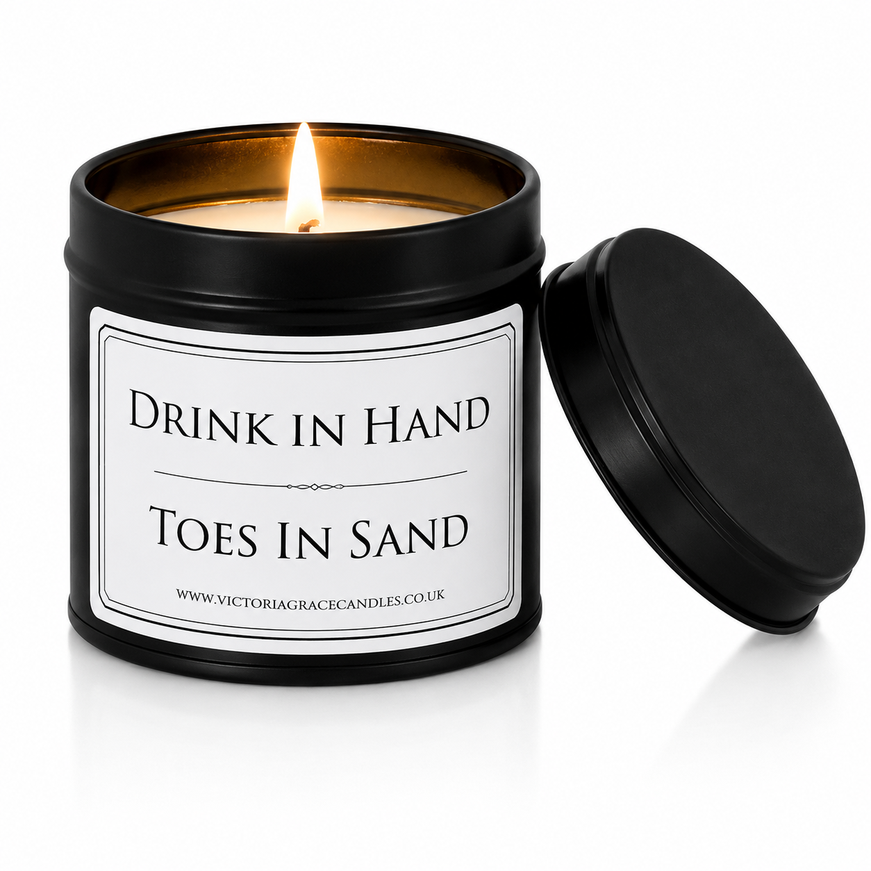 Luxury black soy wax candle with the words "Drink In Hand, Toes In Sand" displayed on a white background with the black lid resting beside the candle.