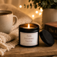Luxury black soy wax candle beside a cosy blanket, coffee mug and warm fairy lights, creating the perfect relaxing evening atmosphere.