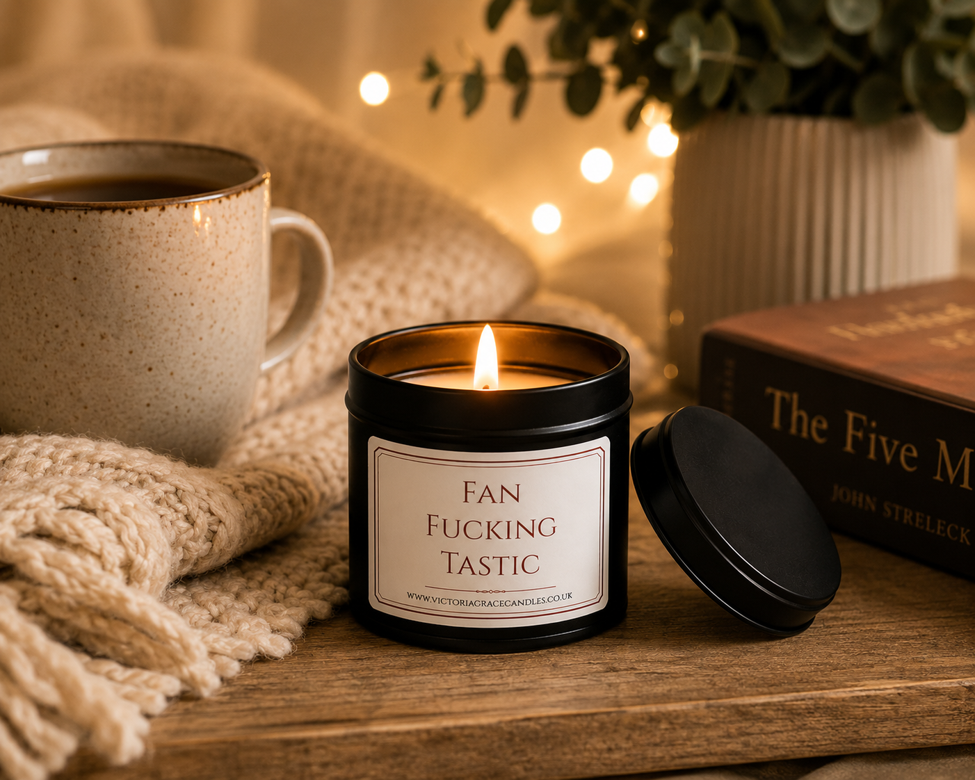Luxury black soy wax candle beside a cosy blanket, coffee mug and warm fairy lights, creating the perfect relaxing evening atmosphere.