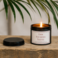 Luxury black soy wax candle displayed on a rustic wooden table beneath tropical green leaves, creating a relaxed and stylish home setting.