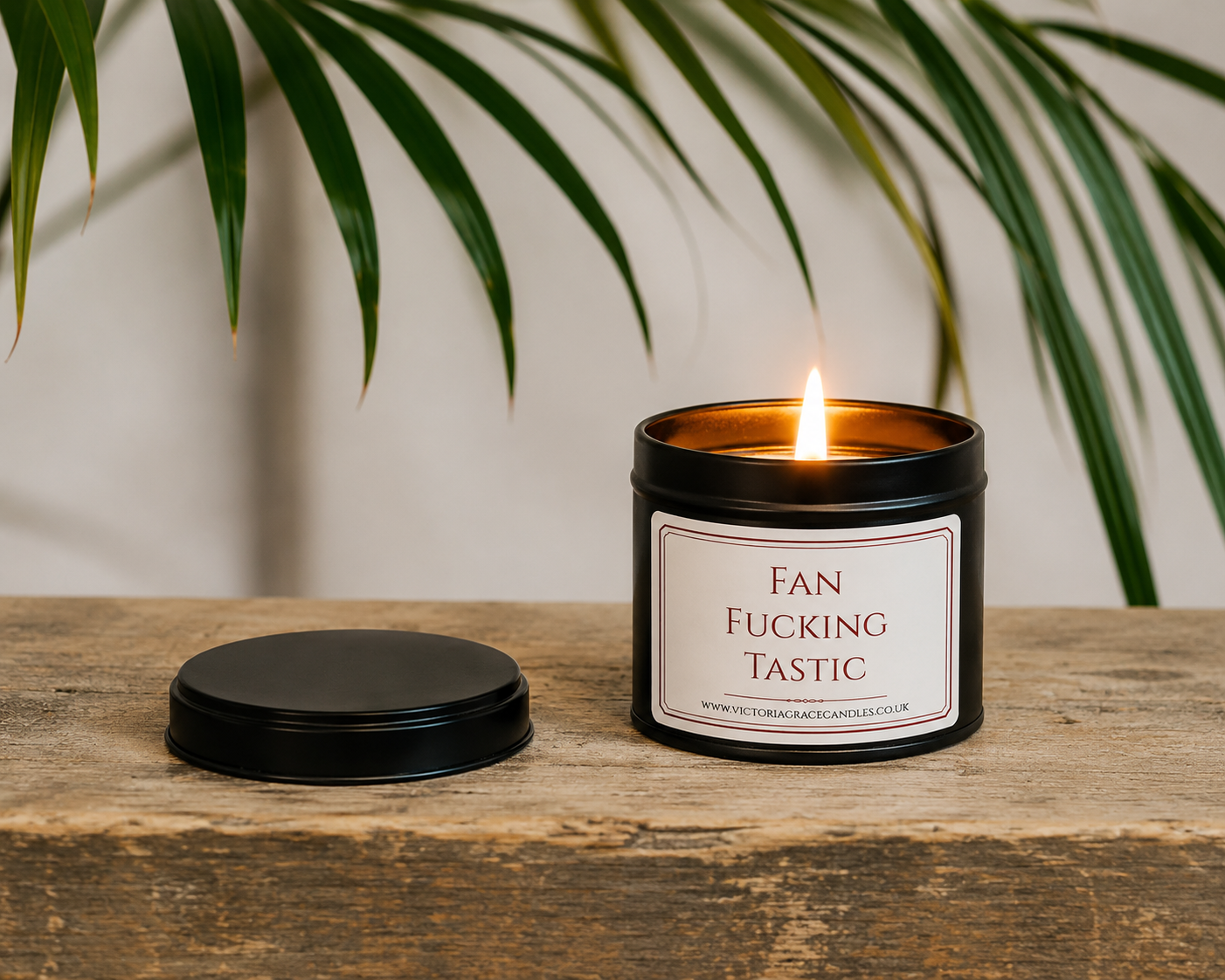 Luxury black soy wax candle displayed on a rustic wooden table beneath tropical green leaves, creating a relaxed and stylish home setting.