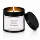 A black metal candle tin with a lit wick and flame, featuring a white label that reads 'FOLLOW YOUR DREAMS' and the website 