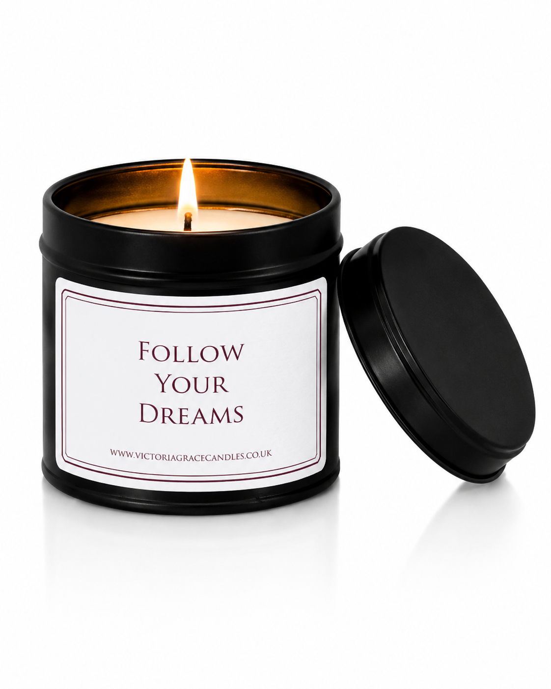 A black metal candle tin with a lit wick and flame, featuring a white label that reads 'FOLLOW YOUR DREAMS' and the website 