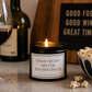 A black candle tin with a lit flame sits on a countertop, surrounded by a wine glass, a bottle, popcorn, and a sign that reads 'GOOD FOOD GOOD WINE GREAT TIMES'. The candle label says 'FRIDAY NIGHTS ARE FOR KITCHEN DISCOS'.