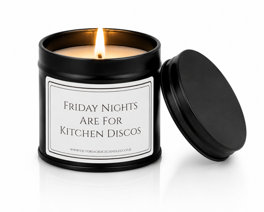 A black metal candle tin with a lit candle and its lid leaning against it on a white background. The front label reads 'FRIDAY NIGHTS ARE FOR KITCHEN DISCOS' with a small website at the bottom.