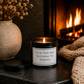 Funny soy wax candle creating a cosy atmosphere beside a glowing fireplace with soft knitted textures and warm lighting.