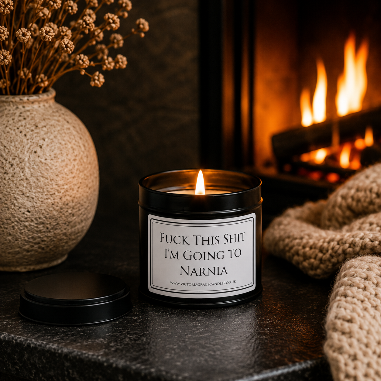 Funny soy wax candle creating a cosy atmosphere beside a glowing fireplace with soft knitted textures and warm lighting.