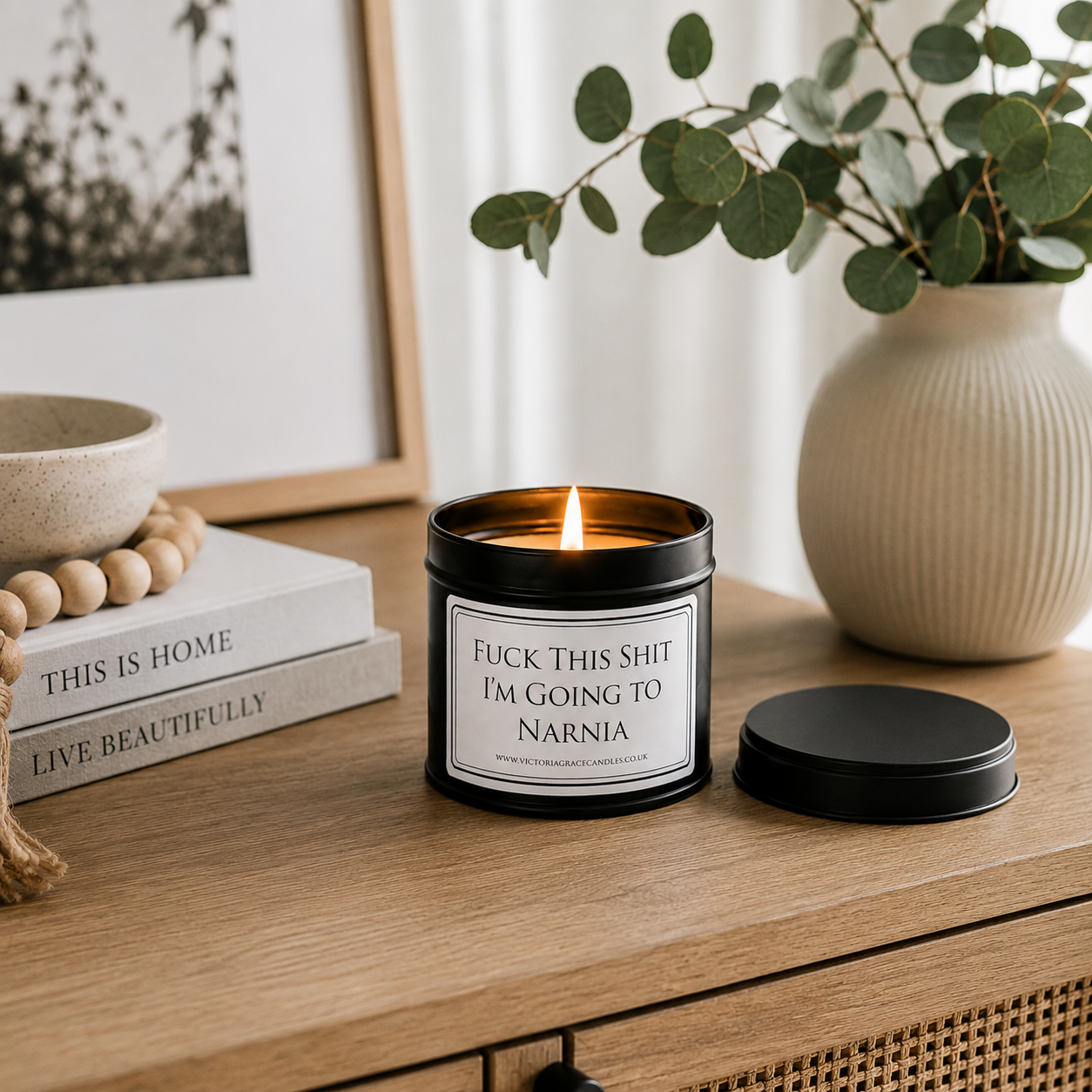 Luxury black soy wax candle displayed on a modern wooden sideboard with eucalyptus, books and neutral home décor.