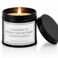 A black metal candle tin with a lit candle and its lid leaning against it on a white background. The front label reads, 'I AM HAPPY TO REPORT THAT MY INNER CHILD IS AGELESS'