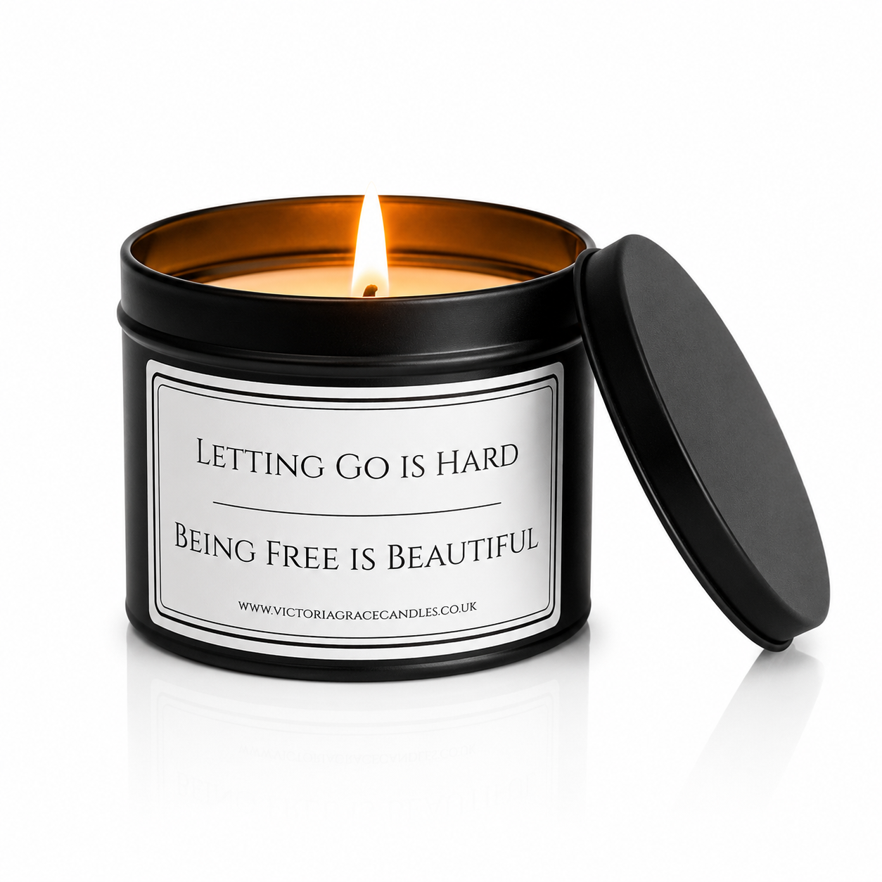 A black metal candle tin with a lit flame, featuring a white label that reads 'LETTING GO IS HARD BEING FREE IS BEAUTIFUL' 