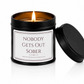 Luxury black soy wax candle with the words "Nobody Gets Out Sober" on a white label, displayed on a white background with the black lid leaning against the right-hand side of the candle.
