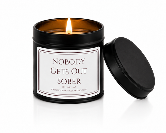 Luxury black soy wax candle with the words "Nobody Gets Out Sober" on a white label, displayed on a white background with the black lid leaning against the right-hand side of the candle.