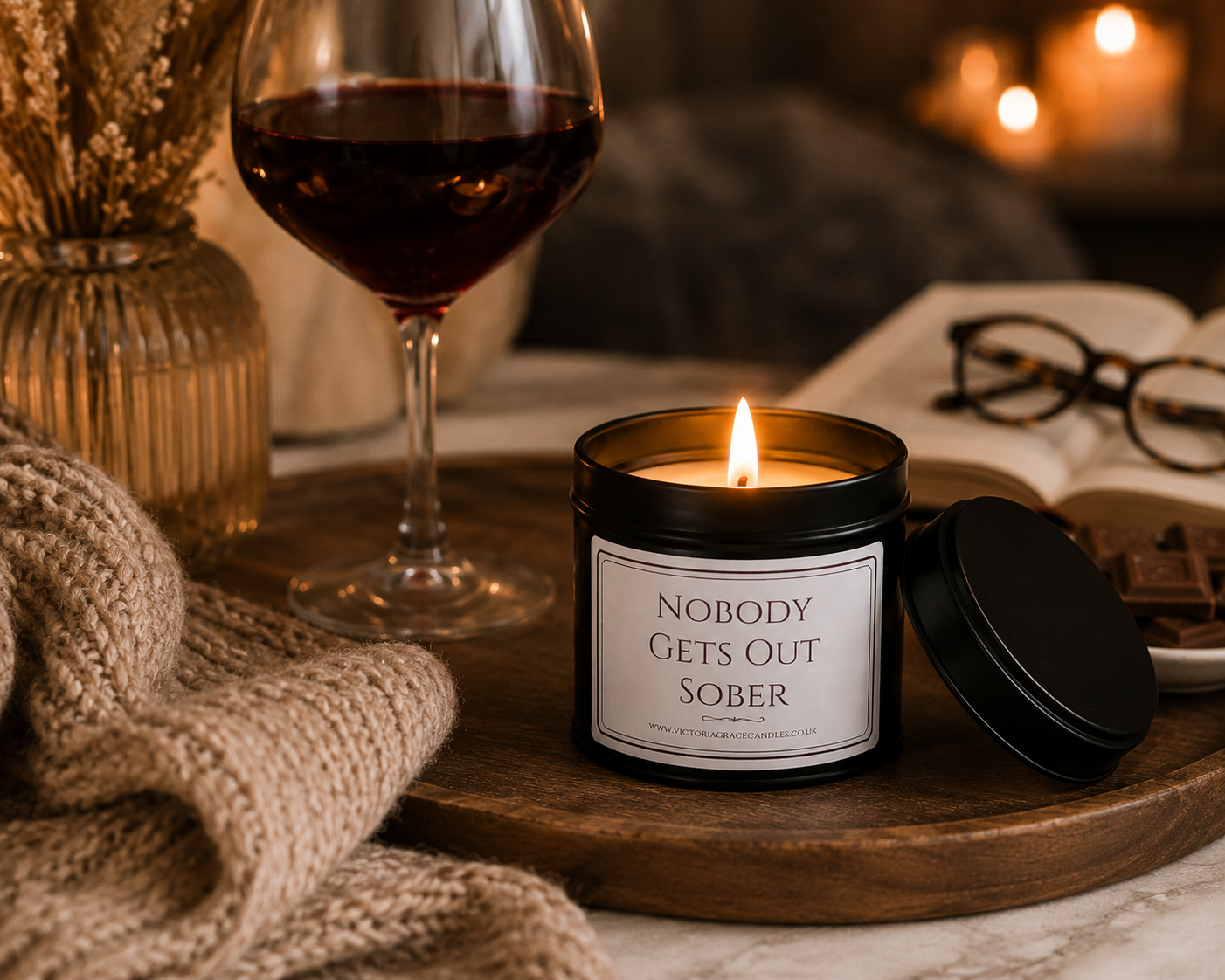 Luxury soy wax candle beside a glass of red wine, chocolates and a soft blanket, creating the perfect relaxing evening setting.