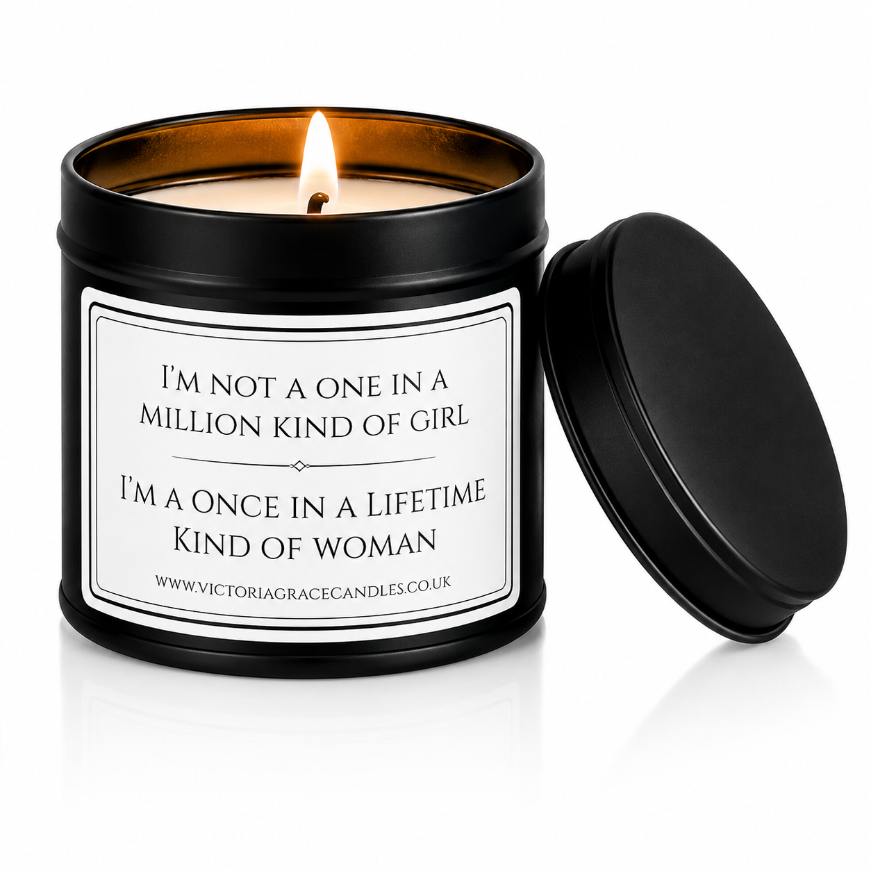 A black metal candle tin with a lit candle inside, shown next to its matching black lid on a white background. The front label reads, 'I'M NOT A ONE IN A MILLION KIND OF GIRL I'M A ONCE IN A LIFETIME KIND OF WOMAN' with the brand Victoria Grace Candles visible at the bottom.