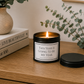 Luxury black soy wax candle displayed on a wooden sideboard with eucalyptus, books and modern neutral home décor.