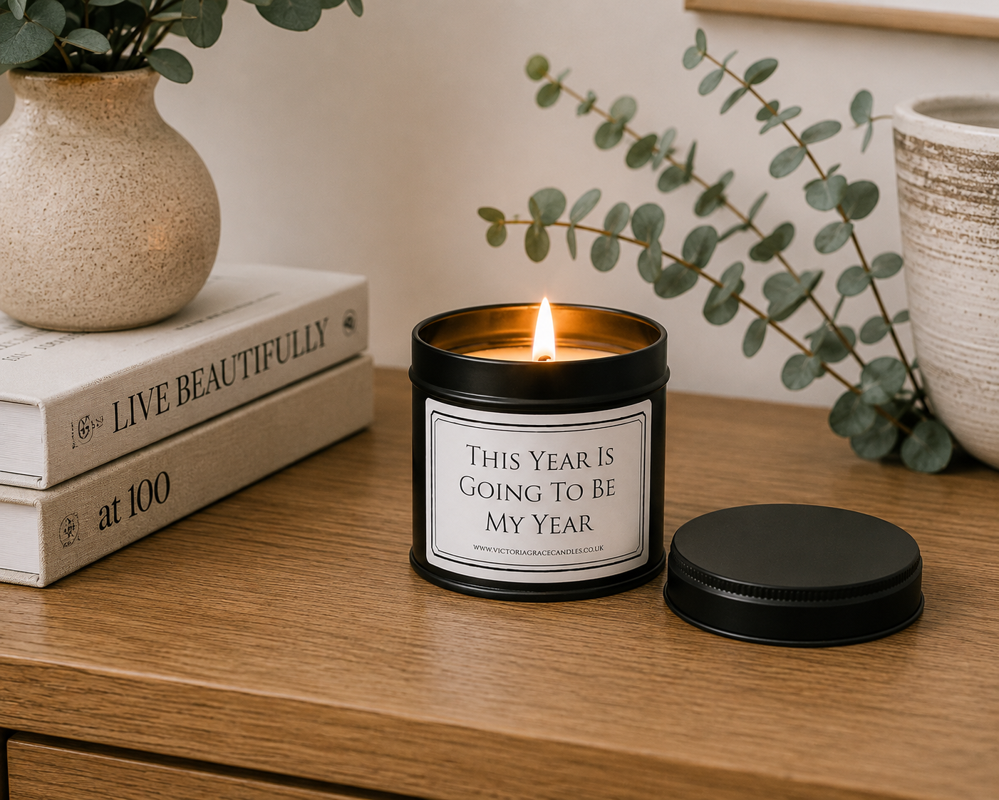 Luxury black soy wax candle displayed on a wooden sideboard with eucalyptus, books and modern neutral home décor.