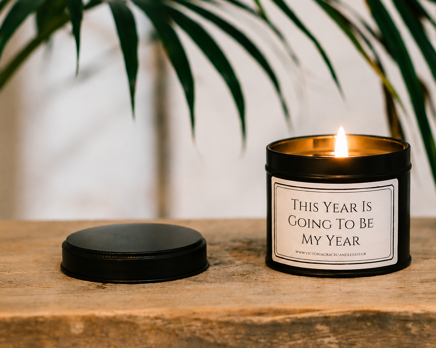 Luxury inspirational soy wax candle displayed on a rustic wooden table beneath tropical green leaves, creating a calm and motivating atmosphere.
