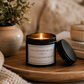 Luxury soy wax candle on a wooden tray surrounded by books, cosy textiles and neutral home décor, creating an inspiring workspace.