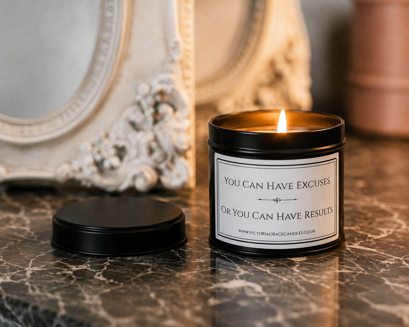 A black metal candle tin with a lit flame sits on a dark marble surface, with its black lid placed beside it. The front label reads, 'YOU CAN HAVE EXCUSES OR YOU CAN HAVE RESULTS' 