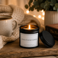 Luxury black soy wax candle beside a cosy blanket, hot drink and warm fairy lights, creating the perfect relaxing evening atmosphere.