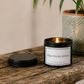 Luxury black soy wax candle displayed on a rustic wooden table with a decorative plant in a relaxed, stylish home setting.